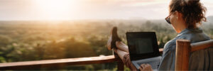 Woman using a laptop on a balcony, in front of a beautiful scene.