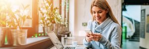 Woman using smartphone and laptop at a lovely bright cafe.